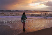 silhouette of a girl. she looks at storm sea in sunset time. waves reach up to her feet