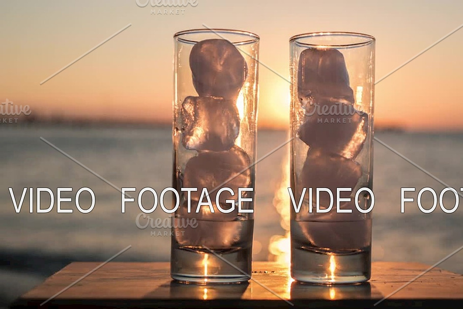 Glasses with melting ice against sea and sunset background