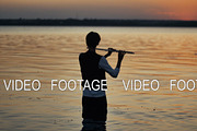silhouette of a flutist playing in the sunset standing in the water