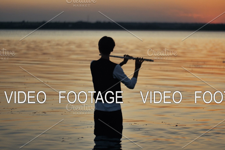 silhouette of a flutist playing in the sunset standing in the water