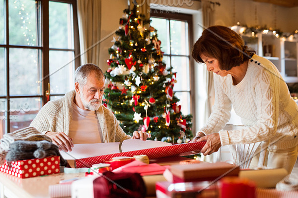 Senior couple in sweaters wrapping Christmas gifts together.