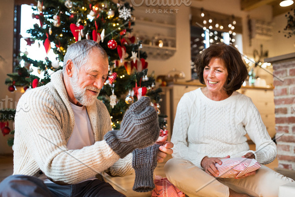 Senior couple in front of Christmas tree enjoying presents.