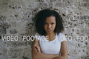 Portrait of angry curly mixed race woman looking into camera nervous on brick wall background