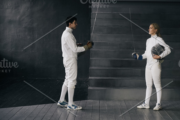Two fencers man and woman have greeting each other and start fencing match indoors