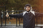 Handsome man in headphones doing warm-up exercise while listening music in winter park