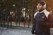 Attractive man in headphones doing warm-up exercise preparing for jogging while listening music in winter park