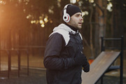 Attractive man in headphones doing warm-up exercise preparing for jogging while listening music in winter park