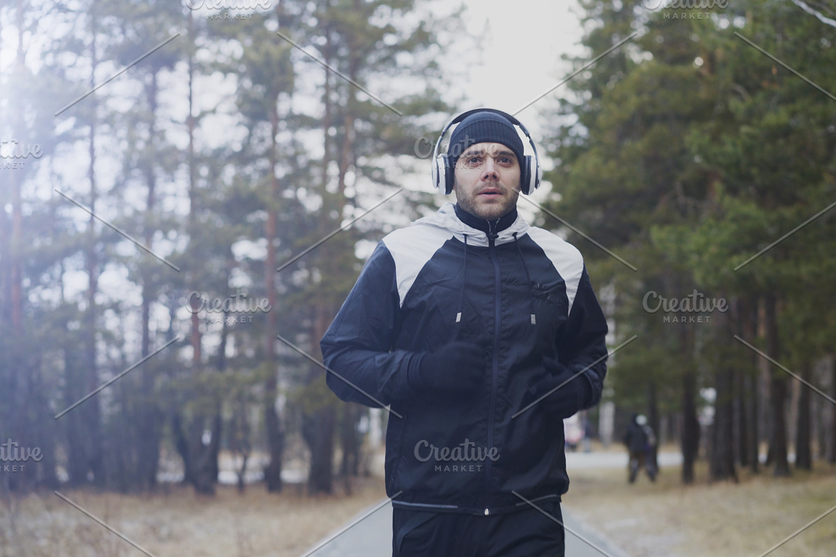 Attractive runner man in headphones jogging while listening music in winter park in the morning in Graphics - product preview 8