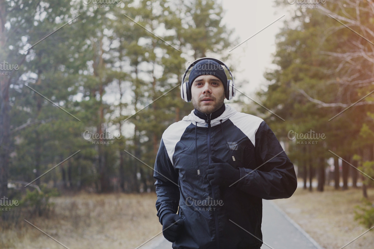 Attractive runner man in headphones jogging while listening music in winter park in the morning in Graphics - product preview 8