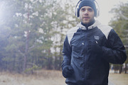 Attractive runner man in headphones jogging while listening music in winter park in the morning