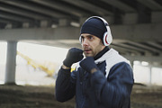 Young man boxer in headphones training punches in urban location outdoors in winter
