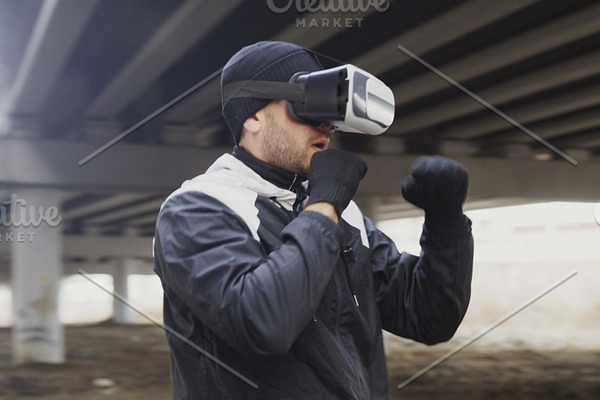 Young man boxer in VR 360 headset training punches in virtual reality fight at urban location outdoors in winter