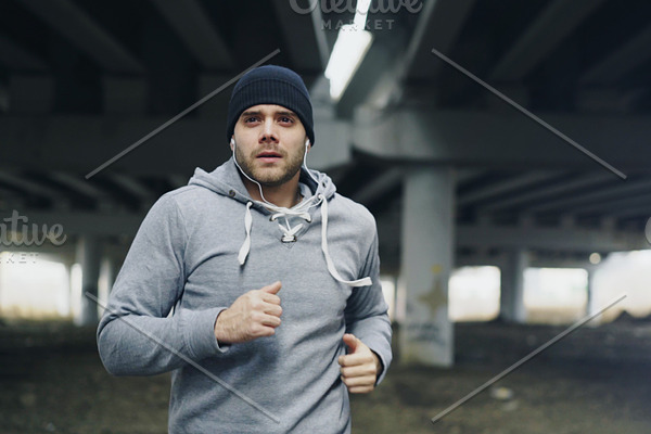 Handsome sportive man runner putting on earphones and starts running at urban outdoors city location in winter