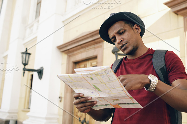 African american tourist man looking into paper city map exploring sightseeings during travelling in Europe