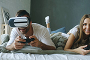 Young couple lying in bed play video games with controller and VR headset