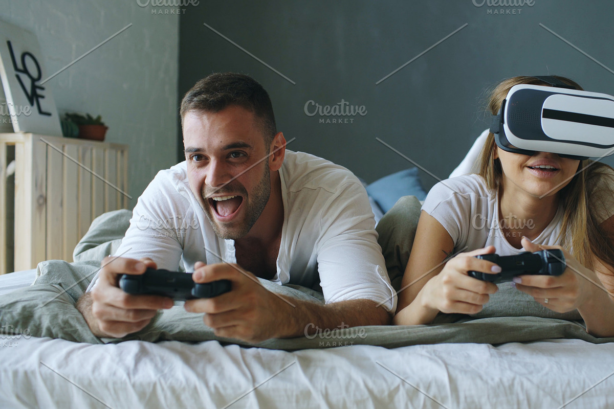 Young couple lying in bed play video games with controller and VR headset in Graphics - product preview 8