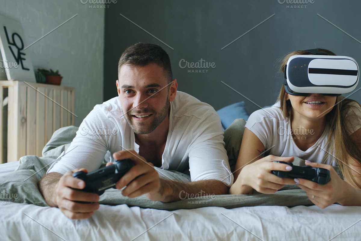 Young couple lying in bed play video games with controller and VR headset in Graphics - product preview 8