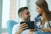 Young cheerful couple using digital tablet computer for online shopping sit on balcony in modern loft apartment