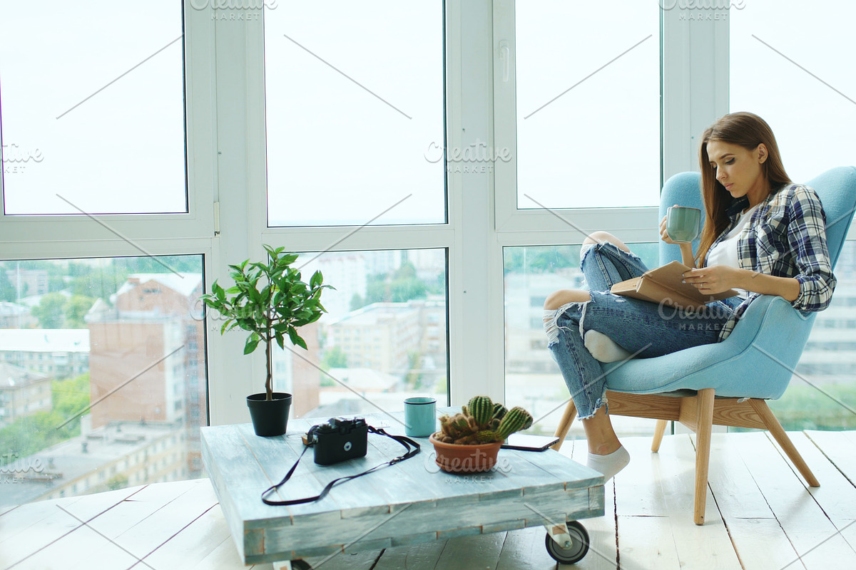 Young attractive woman read book and drink coffee sitting on balcony in modern loft apartment in Graphics - product preview 8