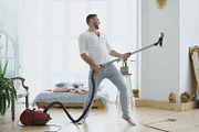 Young man having fun cleaning house with vacuum cleaner dancing like guitarist