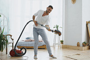 Young man having fun cleaning house with vacuum cleaner dancing