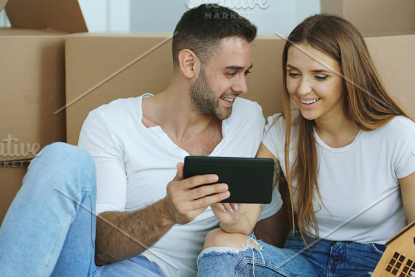 Young couple sitting on floor using tablet computer after reloction in their new home