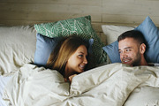 Top view of couple having fun in bed lying under blanket looking each other