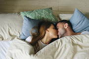 Top view of couple having fun in bed lying under blanket looking into camera and kissing at home