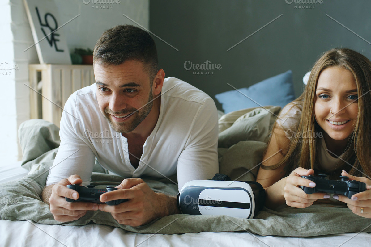 Young couple playing video copmuter games lying in bed at home in Graphics - product preview 8
