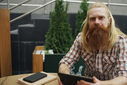 Portrait of young bearded man with tablet computer sitting in cafe outdoors smiling and having relax and resting of work
