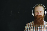 Closeup portrait of bearded young man in headphones listen to music and looking into camera smiling