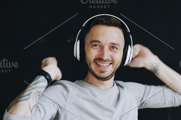 Closeup portrait of young funny man puts on headphones and crazy dancing while listen to music on black background
