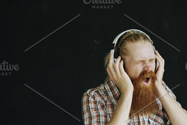 Portrait of bearded young man puts on headphones and dancing while listen to music on black background