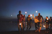 Group of young friends having a beach party. Friends dancing and celebrating with sparklers in twilight sunset