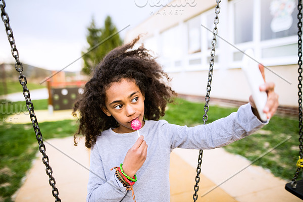 African american girl with lollipop taking selfie with smartphon
