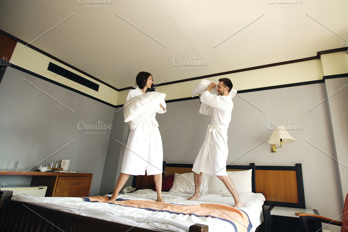 Young happy couple in bathrobe fight pillows and have fun on bed in hotel during their honeymoon vacation in Graphics - product preview 8