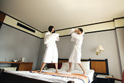 Young happy couple in bathrobe fight pillows and have fun on bed in hotel during their honeymoon vacation