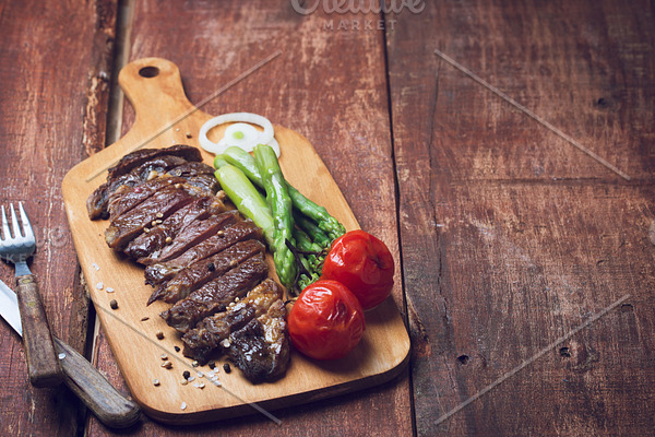 Grilled beef steak with asparaguas and tomatoes on a wooden rustic background