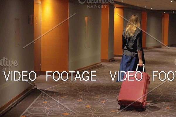 Woman with suitcase walking to the room in hotel corridor