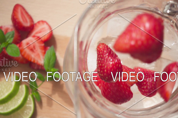 Sliced strawberries fall into a carafe with ice and water slow motion