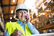 Senior woman warehouse manager or supervisor with smartphone, making phone call.