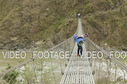 Local men carries a heavy load on suspension bridge over the river in Nepal.