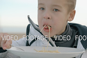 Young boy eating pasta outside