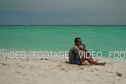 A man sits on a tropical beach.
